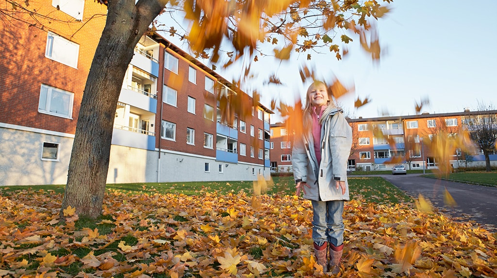 Flicka leker bland höstlöven utanför lägenhetshus.